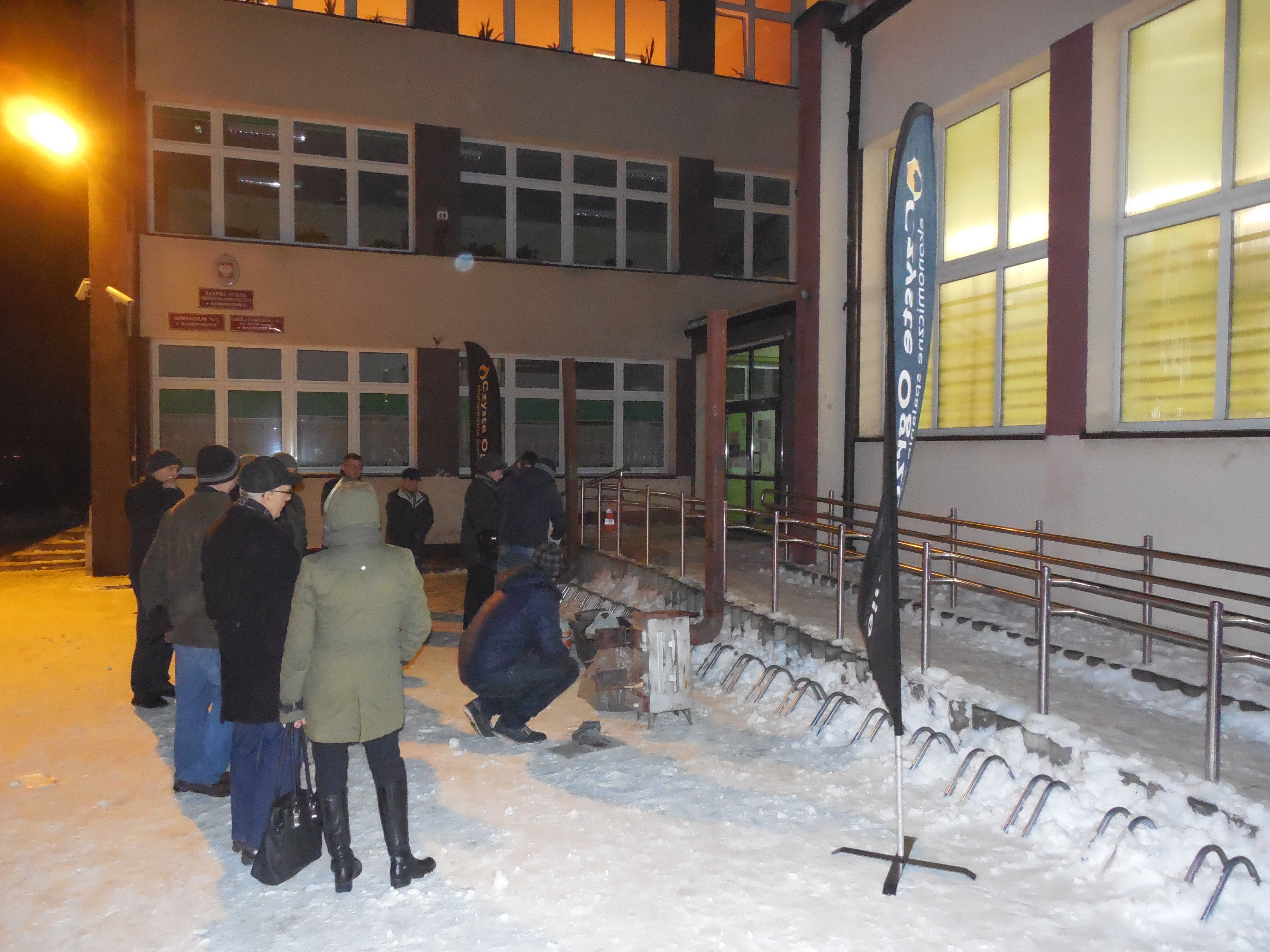 Ludzie przed budynkiem szkoły oglądają piec
