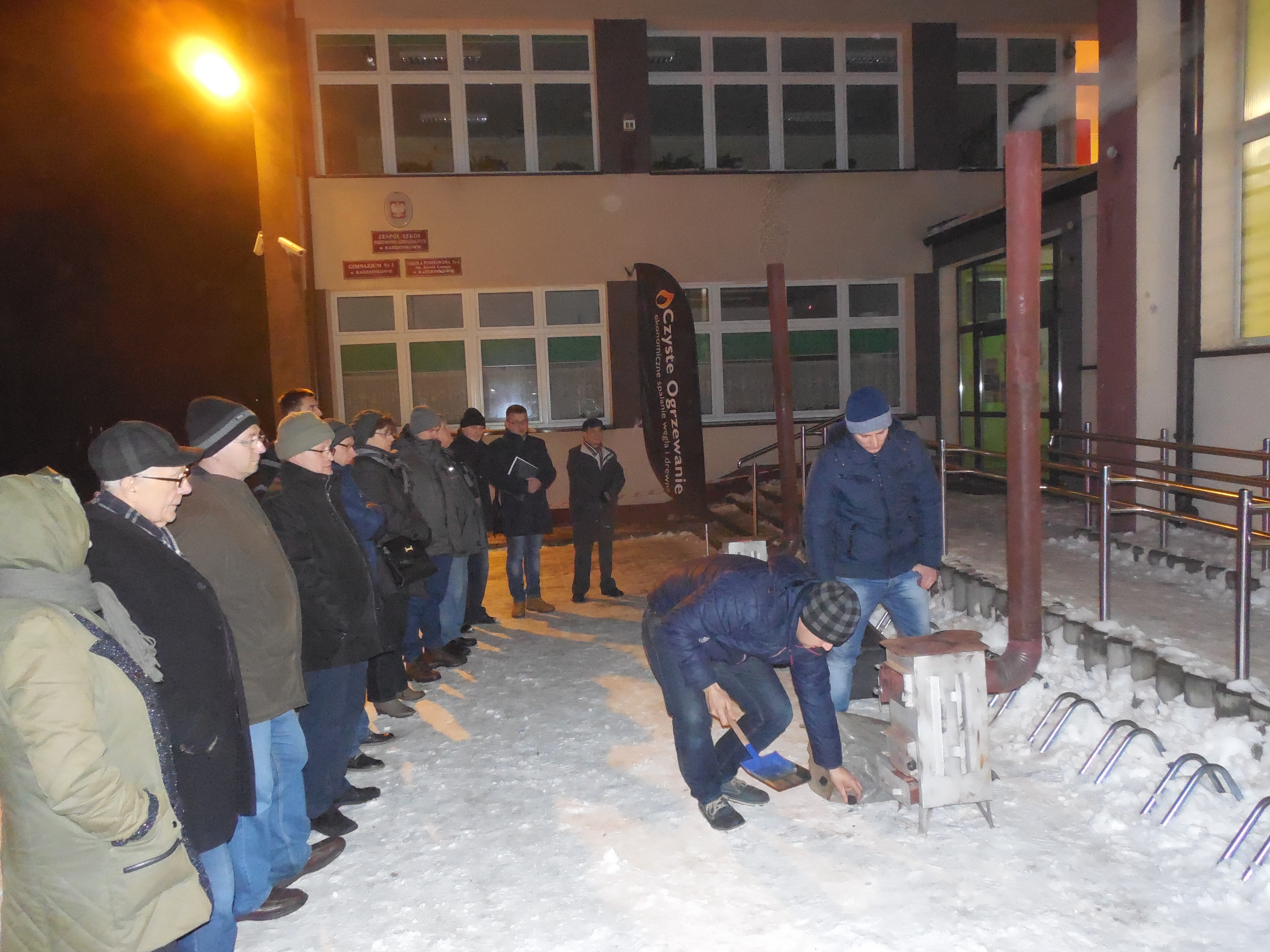Grupa ludzi stoi i patrzy jak jeden Pan sprawdza piec